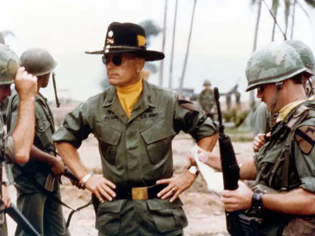 Robert Duvall interpretando al teniente coronel Kilgore, rodeado de jóvenes soldados. Duvall está parado en la mitad, con un gran sombrero negro, gafas oscuras y una pañoleta amarilla