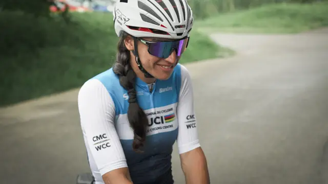 Yulduz était assise sur son vélo et souriait en portant un kit de cyclisme, des lunettes et un casque.