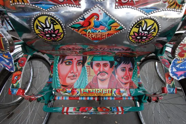 Prikaz zadnjeg dela rikše u Daki, Bangledeš na kojem dominira predstava junaka iz lokalne filmske industrije, Dolivuda. Funkcija dekoracije prevoznih sredstava je višestruka: s jedne strane to je komunikacijsko sredstvo koje izražava ukus, uverenja, humor, kao i prestiž vlasnika, dok s druge strane ukrasi služe da privuku pažnju obiljem različitih ornamenata i motiva.