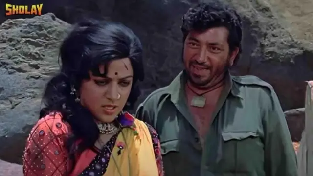 'शोले' चित्रपटातील एका दृश्यात हेमा मालिनी आणि अमजद खान. चित्रपटातील हेमा मालिनीच्या पात्राचे नाव बसंती आणि अमजद खानच्या पात्राचे नाव गब्बर सिंग होते.