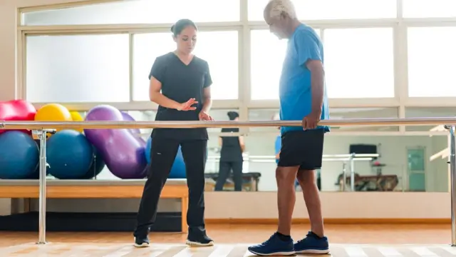 Homem faz exercício caminhando,aposta ganha evertonsalaaposta ganha evertonfisioterapia, observado por profissionalaposta ganha evertonsaúde