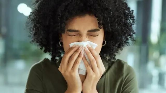 Uma mulher segurando um lenço no nariz enquanto espirra