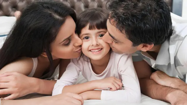 युवा माता-पिता अपने बच्चे को चूम रहे हैं, परिवार एक साथ आनंद ले रहा है