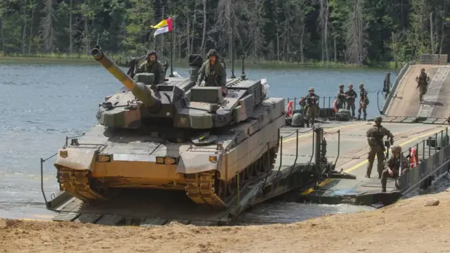 迷彩柄の戦闘服を着た兵士がポーランドの湖で、渡河作戦を想定した訓練を行っている。兵士2人が乗った戦車が陸地に上がろうととしている。後ろには複数の兵士が立っている