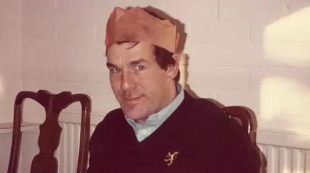 عکس رانی لاکوود با کلاه کاغذی قرمز مخصوص کریسمس، پیراهن آبی و ژاکت یقه هفت سرمه‌ای. چشمان آبی روشن دارد و لبخند می‌زند