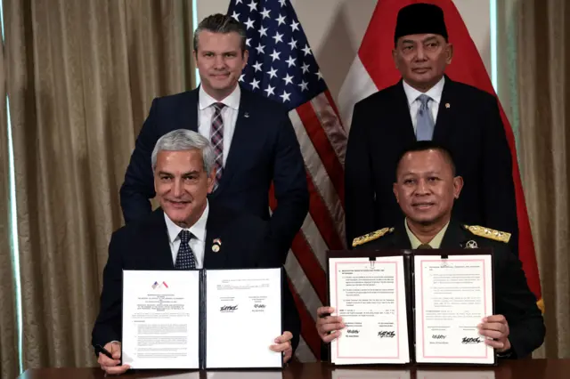 US Defense Secretary Pete Hegseth and Indonesia's Defense Minister Sjafrie Sjamsoeddin stand behind a desk as seated colleagues hold up a Memorandum of Understanding 