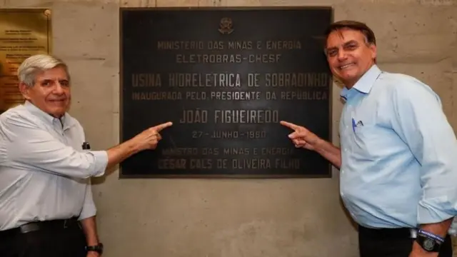 Heleno e Bolsonaro sorrindo enquanto apontam para placa de inauguração de obra com nome de João Figueiredo
