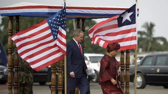 El expresidente estadounidense George W. Bush junto a la ex presidente de Liberia Ellen Johnson Sirleaf junto a las banderas de EE.UU. y de Liberia. La de Liberia tiene menos franjas rojas y blancas que la bandera estadounidense, y lleva una sola estrella blanca sobre el cuadro azul.