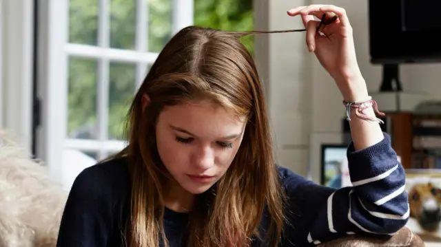 Uma menina enrolando uma mechasportnet net apostas onlinecabelo enquanto olha para celular