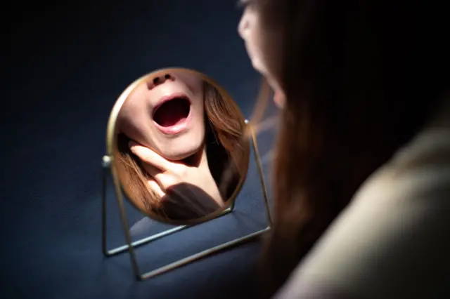 Mulher checando as amígdalas em espelho