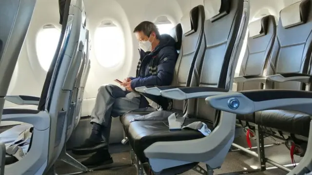 ஜெர்மனி ஹம்பர்கில் ஆளே இல்லாத விமானத்தில் முகக் கவசத்துடன் தன்னந்தனியாக உட்கார்ந்திருக்கும் ஒரு பயணி.