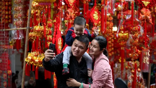 越南河内某售卖春节装饰品商店前一个家庭举起手机自拍（2/2/2019）