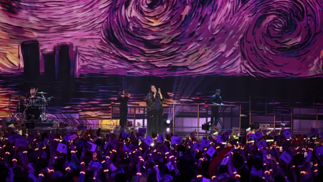 Катарска представница Дана ал-Мир насупа на Интервизији, иза ње је видео бим на којем су огромне уметничке инсталације, а испред ње публика