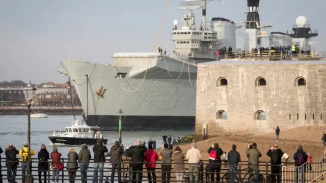 有许多当地民众，站在海岸边为这艘前皇家海军旗舰送行。