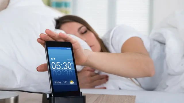 Mujer acostada con el celular en la mesa de noche