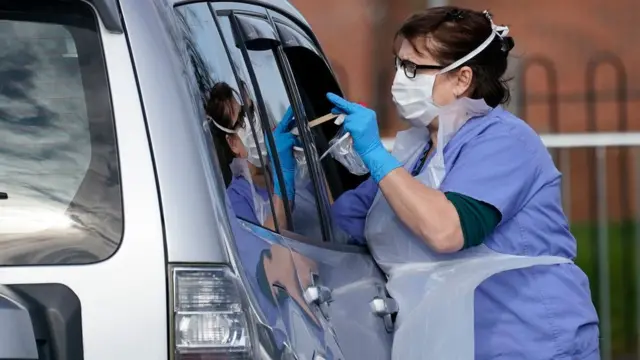 A nurse swabs a person in a car to check if they have coronavirus