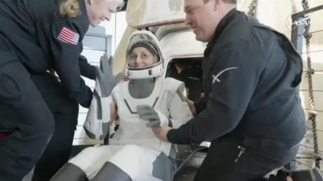 Suni sorrindo ao deixar cápsula, auxiliada por outras pessoas