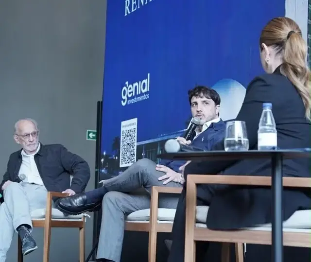 Renan Santos durante encontro com clientes da Genial Investimentos, com o economista José Márcio Camargo ao fundo, em 10 de junho de 2026