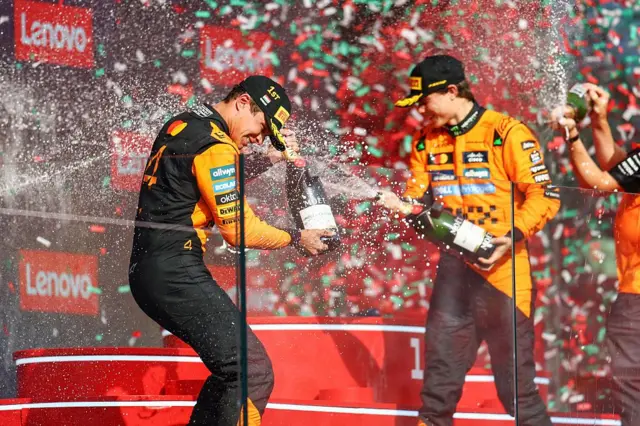 Dois pilotos no pódio estourando champanhe e comemorando