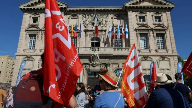 Протестующие с красными флагами Французской коммунистической партии перед старинным зданием мэрии во время демонстрации в Марселе