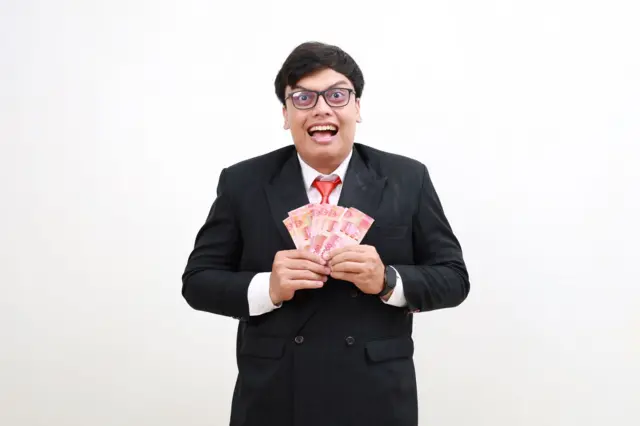 Seorang pria memegang segepok uang rupiah.