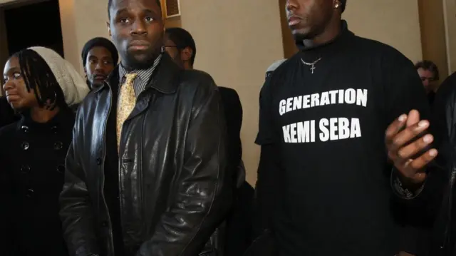 Seba se tient à gauche et un homme portant un t-shirt noir avec l'inscription « génération Kemi Seba » à droite.