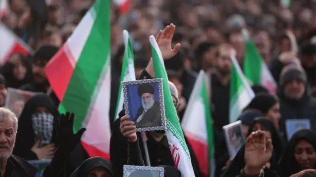 ハメネイ師の遺影や国旗を手にした黒衣の群衆