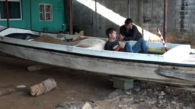 Un hombre dentro de un barco en tierra conversa con otro que está fuera del bote.