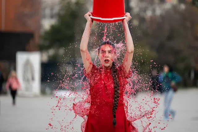 La artista y activista feminista Saranda Sadikaj, conocida como "Ms. Indefinite", con sede en Kosovo, se echa un cubo de agua de colores durante su actuación en Pristina.