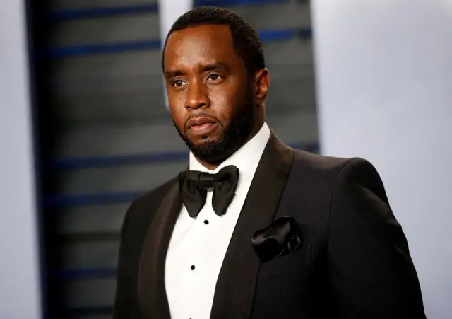 Diddy posando com roupa de gala, em pé em evento; ele tem olhar sério