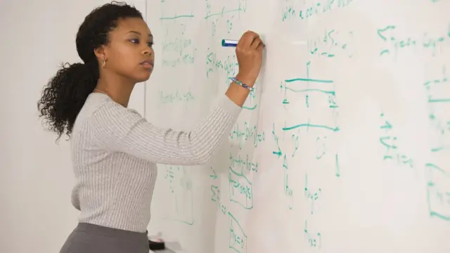 Una mujer escribe fórmulas matemáticas en una pizarra