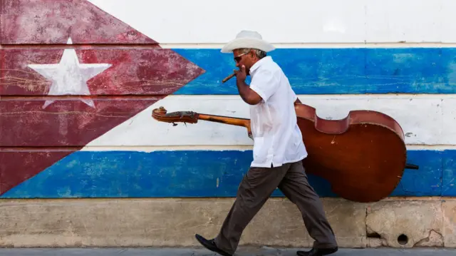 Homem fuma charuto em frente a bandeira de Cuba pintada no mural