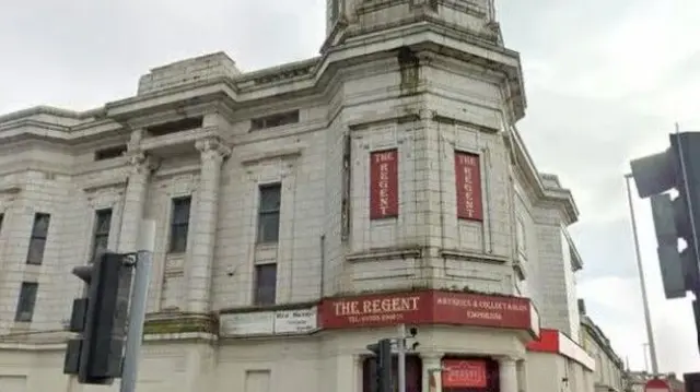 Vista exterior del edificio Art Decó de azulejos blancos con un cartel rojo de The Regent