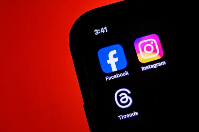 Kırmızı fonda bir telefon, ekranda Facebook, Instagram, Threads ikonları var