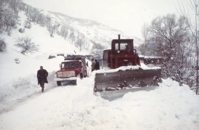 Karlı yolları açmaya çalışan bir kar küreme aracı ve yanında duran bir kamyon 