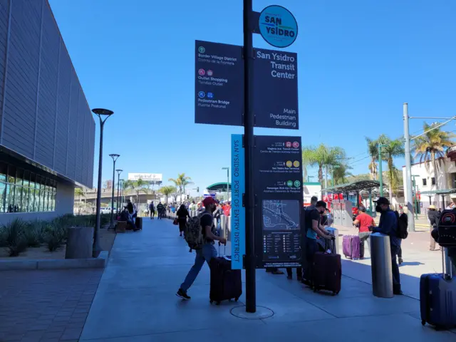 Personas con maletas hacen fila al ingreso a EE.UU. desde México.