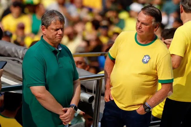 Tarcísio e Bolsonaro em pé, observando manifestação; eles estão vestindo verde e amarelo, cores associadas ao bolsonarismo