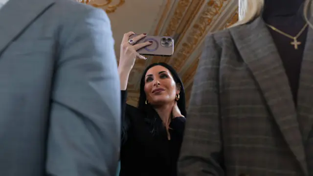 Activista politică de dreapta Laura Loomer participă la o ceremonie de inaugurare a drumului de la Mar-a-Lago pe 16 ianuarie 2026 în Palm Beach, Florida. Ea are parul închis la culoare și poartă o bluză neagră și cercei aurii. Ea ține în mână un telefon și pare să facă o fotografie.