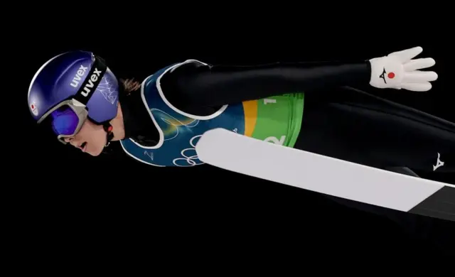 黒いウェアの小林が空中で深い前傾姿勢を取りながら前方を見ている