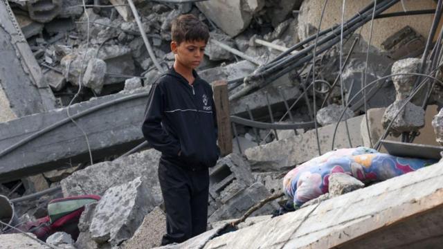 Un niño mira los escombros de un edificio.