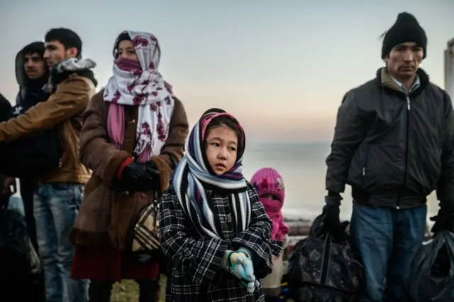 Deniz kıyısında bekleyen bir kız çocuğu, kadın ve erkekler
