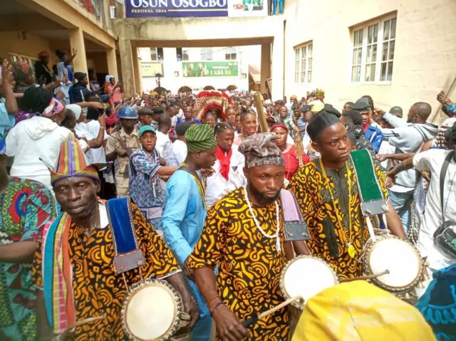 Arugba n ru igba lọ si oju odo Ọṣun pẹlu awọn onilu niwaju rẹ