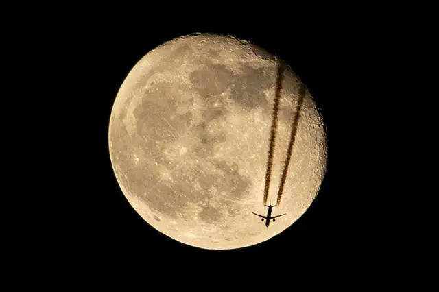 طائرة تحلق فوق البصرة ، في جنوب العراق ، مظللة أمام تراجع القمر في 18 أبريل/نيسان 2022