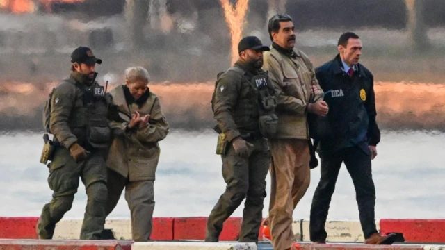 Kahverengi kıyafetler giydirilmiş Maduro ve eşi, kamuflajlı ABD güvenlik görevlilerinin arasında yürüyor. Eşinin yüzünde morluklar var.