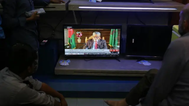 প্রধান নির্বাচন কমিশনার কেএম নুরুল হুদার টেলিভিশন বিবৃতি শুনছেন সাধারণ মানুষ।