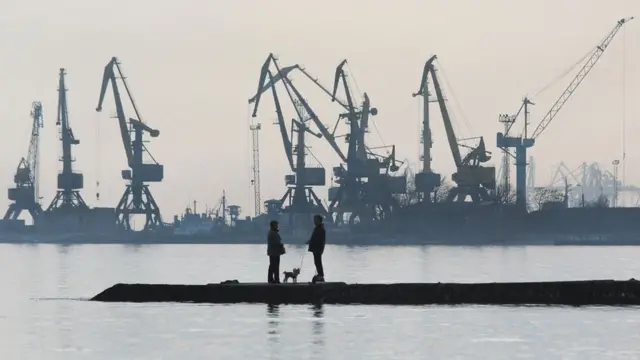 A couple walks a dog on a pier at a coast of the Sea of Azov in Ukraine's industrial port city of Mariupol on February 23, 2022