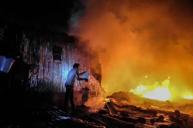 A man struggles to put out a night fire that razed down homes, leaving most families homeless during late-night hours in Kibera, Nairobi. Residents of Kibera Slums experienced another loss as they were caught unaware by a fire that occurred late in the night, razing down twenty homes, leaving most locals homeless and with nowhere to turn to. The fire eruption was due to tangled wires from illegal electric connections.
