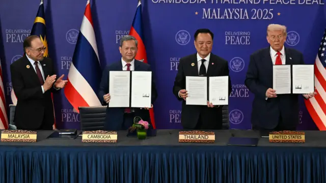Przywódcy USA, Tajlandii i Kambodży trzymają oficjalne podpisane dokumenty, a czwarty mężczyzna po lewej, przywódca Malezji, klaszcze. W tle widać flagi tych państw.