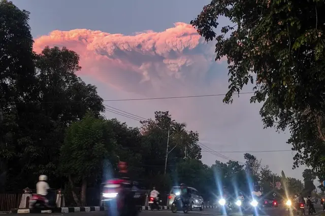Pengendara motor melintas berlatar belakang awan panas erupsi Gunung Lewotobi Laki-laki di Maumere, Kabupaten Sikka, Nusa Tenggara Timur, Selasa (17/06).