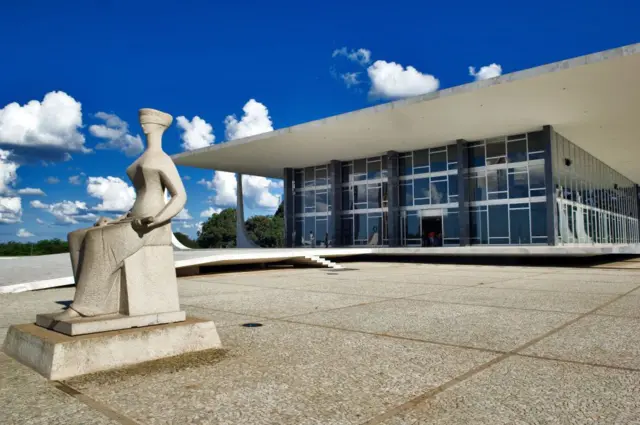 Imagem da área externa do Supremo Tribunal Federal, durante o dia, com estátua que representa a Justiça